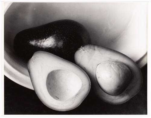 Black-and-white close-up of a bowl of avocados, one cut open and displaying the pit