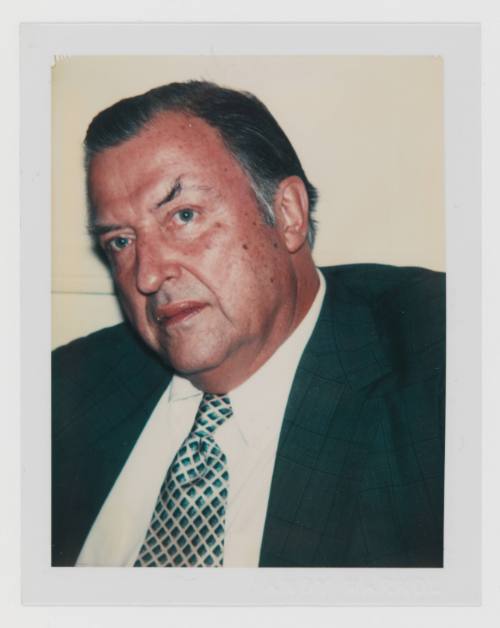 Polaroid portrait of man with graying hair and medium-light skin tone wearing a ring, suit, and tie