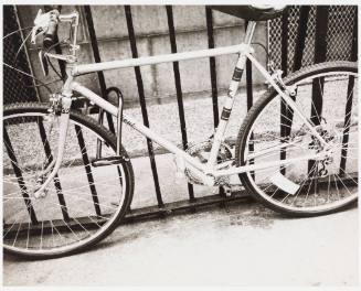 Black-and-white photo of bicycle locked to metal fence