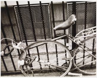 Black-and-white photo of bicycle locked to metal fence