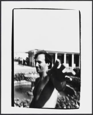 Black-and-white blurry photo of shirtless man smiling and reaching hand out towards camera