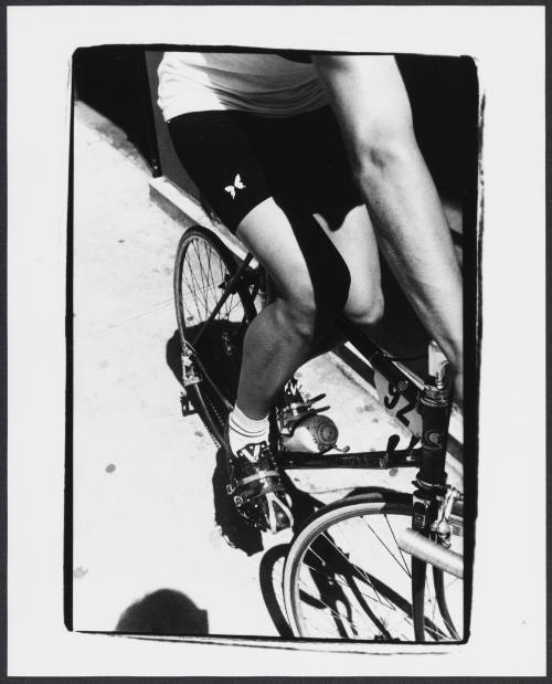Black-and-white close-up photo of man on a bike, seen from the side, riding on a sidewalk