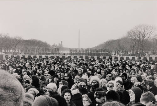 A crowd of female-presenting people stand with the Washington Monument in the background.