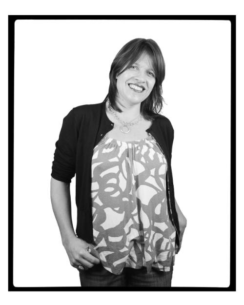 Portrait of a woman with dark hair, wearing jeans and patterned shirt, smiling and facing viewer