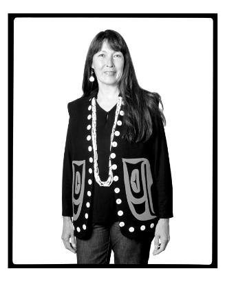 Portrait of a woman with long, dark hair wearing a blazer with buttons and Indigenous motifs