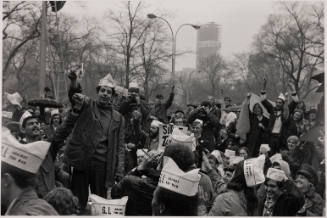 A group of young male-presenting people wearing white paper hats proudly burn small pieces of paper.