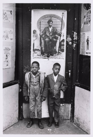 2 Black boys in a doorway beneath an iconic photo of Huey Newton.