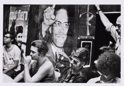 Four people sit in chairs with their backs to posters of Malcom X and Fidel Castro.