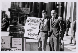 Two men stand beside each other and a sign that reads “FORTUNE employees against WAR PROFITS”.