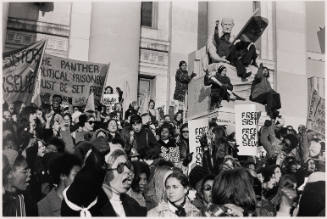 A crowd of female presenting people stand on the steps of a court house with posters and banners.