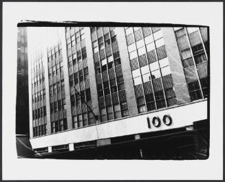 Black-and-white close-up of facade of mid-century building with the building address “100” at lower 