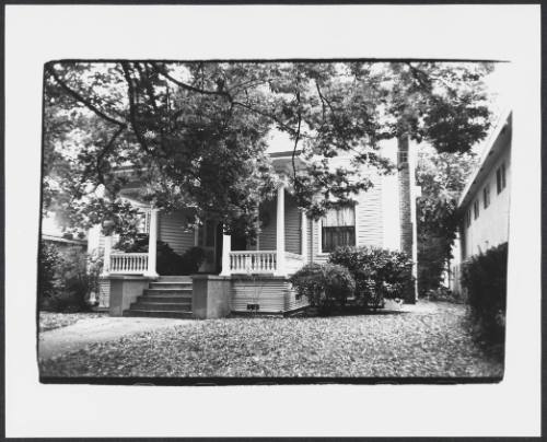 Tree covering a view of a late 19th or early 20th century clapboard-sided house with porch 