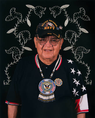 Man in patriotic attire stands in front of black background embellished with beaded floral designs