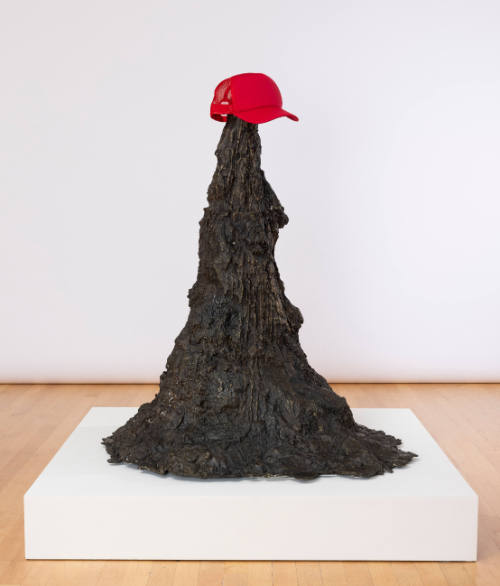 Tall, textured bronze mound that expands at bottom, with red baseball cap sitting on top