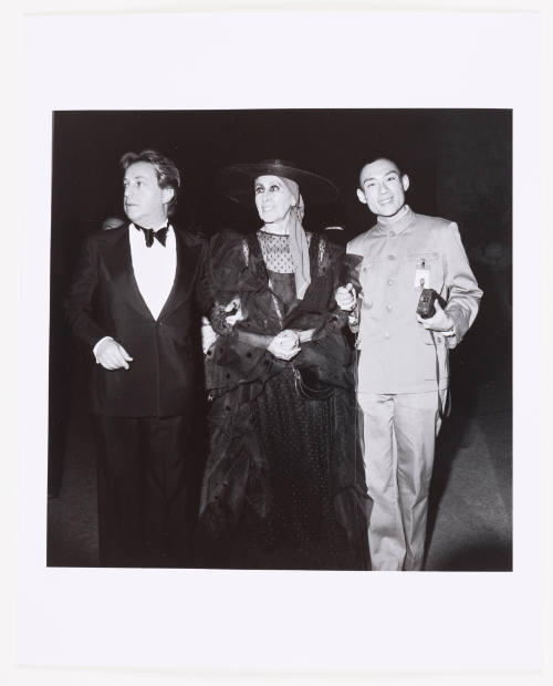 A woman wearing a large hat and dress is flanked by the artist and another man wearing a tuxedo