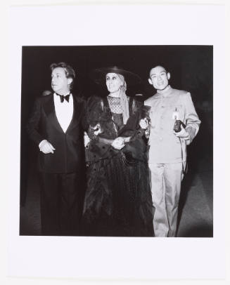 A woman wearing a large hat and dress is flanked by the artist and another man wearing a tuxedo
