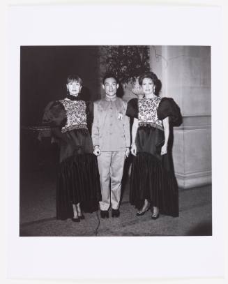 The artist wears a Zhongshan suit and is flanked by two women wearing identical designer dresses