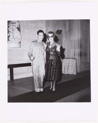 Black-and-white photo of man in Mao suit with woman wearing formal dress and sunglasses in a museum