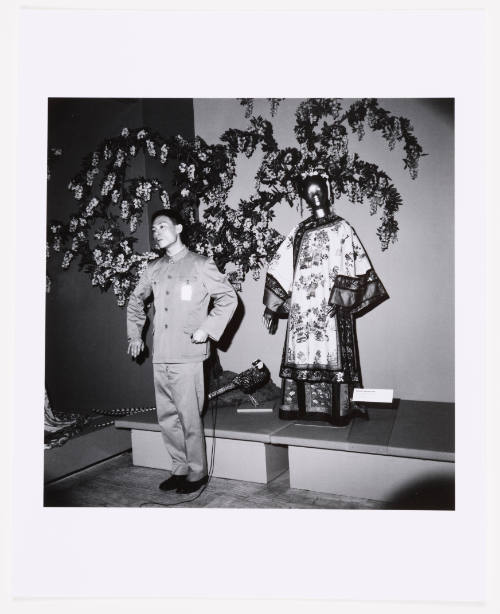Black-and-white photograph of male-presenting person posing with mannequin in Chinese silk robe.