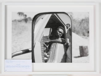 Photo taken in rearview mirror, dark-skinned man in car facing light-skinned woman standing outside