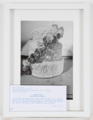 Black-and-white photo of a three-tiered round wedding cake with roses spiraling down the side