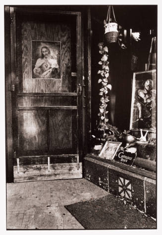 Exterior of wooden door with a poster of Christ adjacent to storefront altar display with a painting