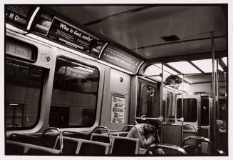 Black-and-white photo inside subway car with seated person face buried in their hands