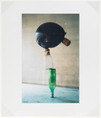 Still life of a balloon balanced atop a jar which in turn is balanced on an inverted wine bottle