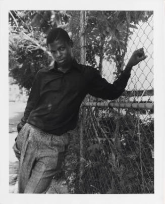 Portrait of a young, fashionably dressed young man with dark skin tone posing against a fence