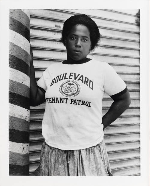 Portrait of a young woman with dark skin tone in a graphic t-shirt and skirt posing against a wall