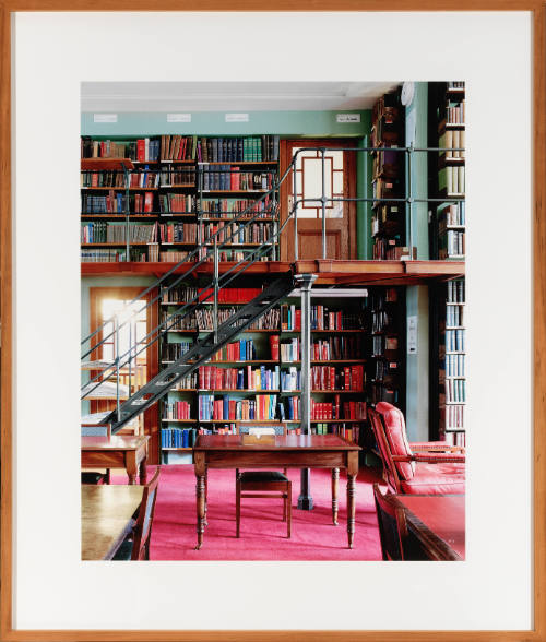 Brightly lit room containing a wall of books, staircase, and tables