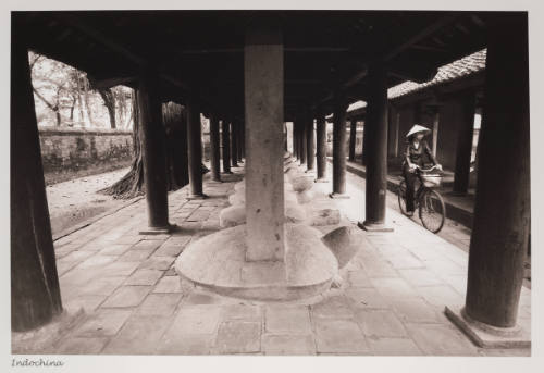 Black-and-white photo of person riding bike near structure with columns atop large turtle sculptures