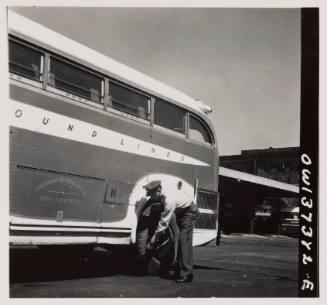 Randy Pribble, a bus driver for the Pennsylvania Greyhound Lines, Incorporated, checking tires on a bus by thumping them before taking it out on a run.  Since there are two tires on the back, the sound is the best way of telling if one of them is flat.  Columbus, Ohio