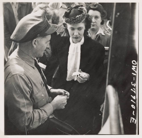 A light-skinned woman hands her bus ticket to uniformed man with a line of people waiting behind the