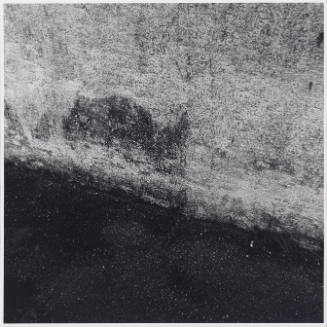 Close-up black-and-white photograph of area where ground meets exterior wall at a diagonal