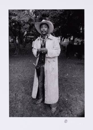 Full-body view of Black man who wears cowboy attire, such as a hat, boots and gun holstor