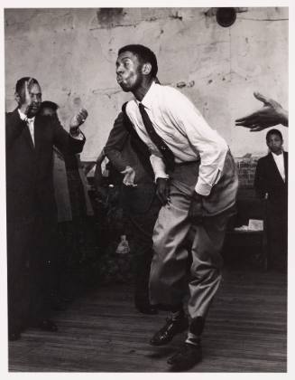 Black-and-white photo of an African-American man dancing and people around him clapping