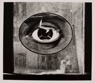 Black-and-white photo of large, painted eye encircled by oval frame, seen through a window