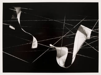 Black-and-white photo of two strands of paper woven through floating, intersecting strings