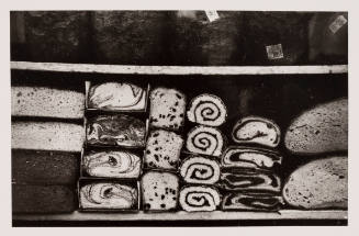 Black-and-white close-up photo of bakery window shelf stacked with sweet and savory breads