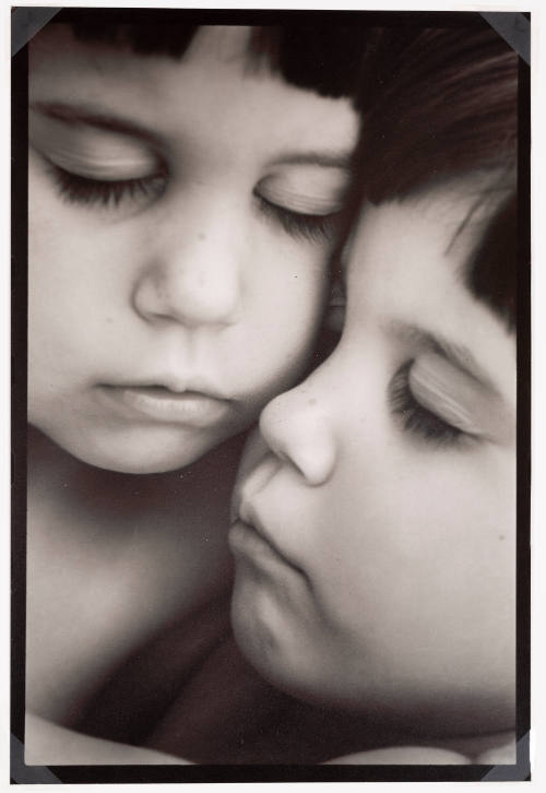 Close-up photo of two young children with light skin tone posed cheek-to-cheek with eyes closed