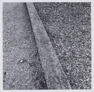 Black-and-white photo of a curb running vertically with asphalt on one side and gravel on the other