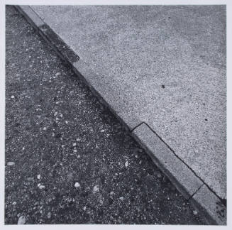Photograph of ground with diagonal division between dirt and rocks on left and concrete on right