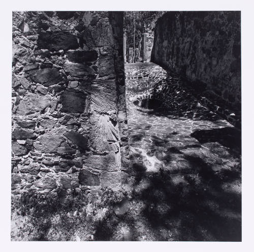 Tight black-and-white photograph of cobblestone enclosure with gaping drain hole and ominous shadows
