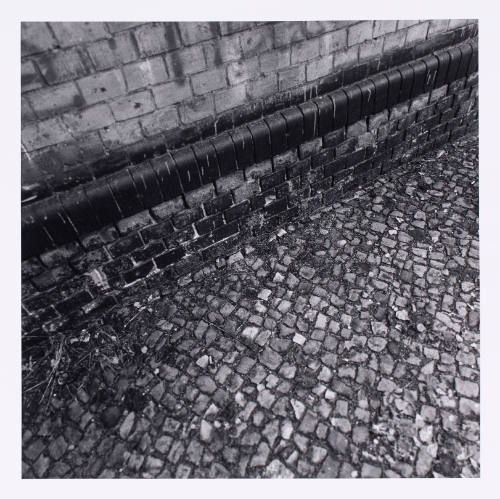 Close-up black-and-white photograph of a worn cobblestone street meeting brick wall