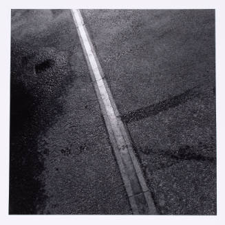 Black-and-white close-up photograph of  paved ground with a slightly raised vertical line at center