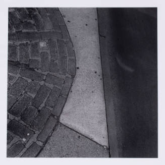 Close-up black-and-white photograph of a sidewalk with a circle of bricks at left and curb at right
