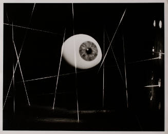 Black-and-white photo with floating eyeball against dark background surrounded by white strings