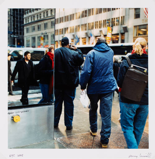 Photo of street scene with people walking down sidewalk, reflective building on left side of frame