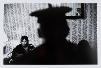 Black-and-white photo of police officer, their face reflected in a mirror, facing seated woman